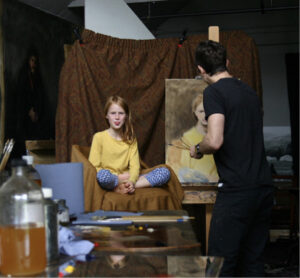 A photo showing a young girl sitting for a portrait painter Daniel J Yeomans